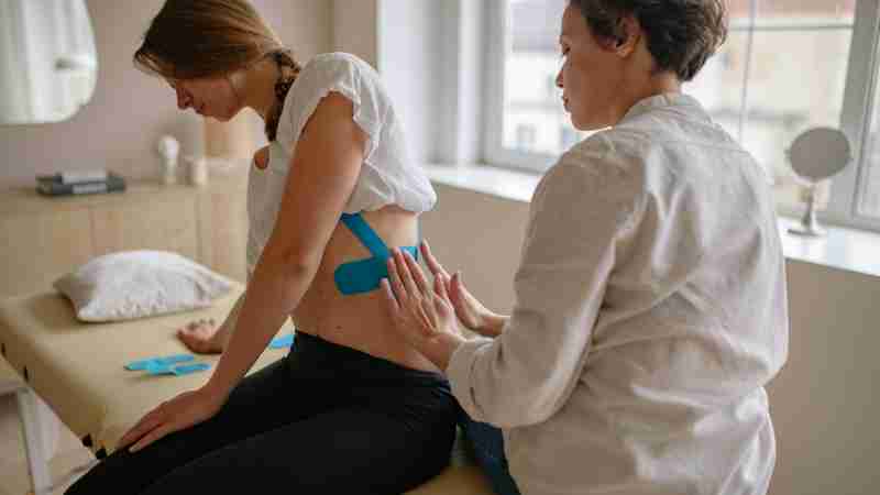 Chiropractor applying kinesiology tape to a woman's rib in a therapy session., tags: van de en - pexel