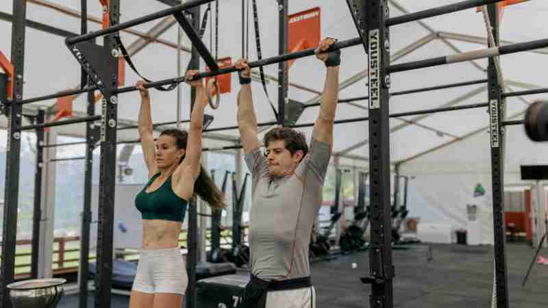 Two adults performing pull-ups in a gym, showcasing strength and fitness focus., tags: naar door de - pexel