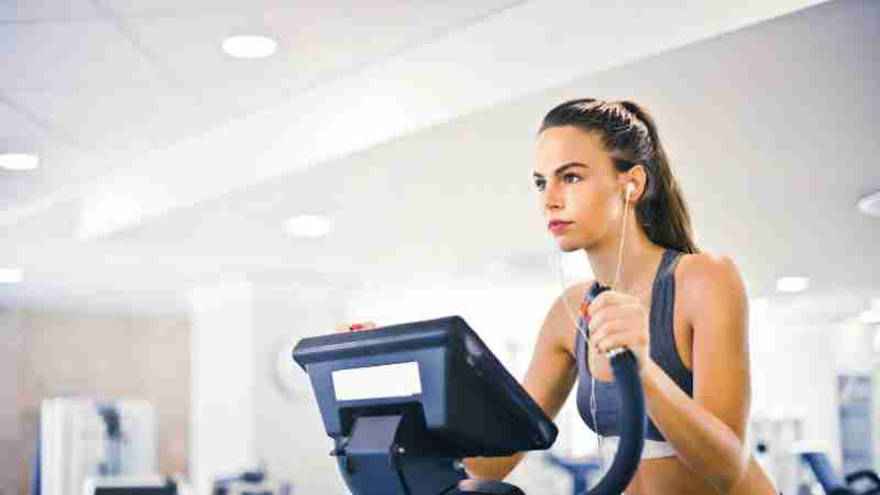 Serious fit woman in earphones and activewear listening to music and running on treadmill in light contemporary sports center, tags: je - pexel
